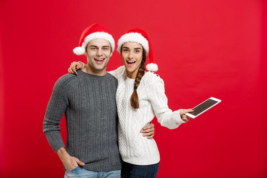 Christmas concept - Happy young couple in christmas sweaters holding digital tablet.