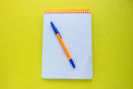Notepad with an orange spiral and an orange pen, on a yellow background. top view copy space.