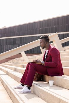 elegant african businessman works with his laptop sitting on a staircase in the city, technology and remote work concept, copy space for text