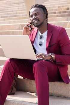 african businessman works with computer laptop and phone sitting on city stairs, technology and remote work concept