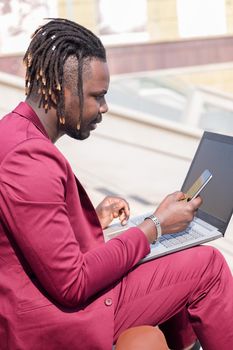 vertical photo of an elegant black businessman working outdoors with laptop and phone, technology and remote work concept