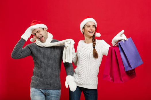 Christmas Concept - Beautiful girlfriend force her boyfriend to go shopping over red christmas background.