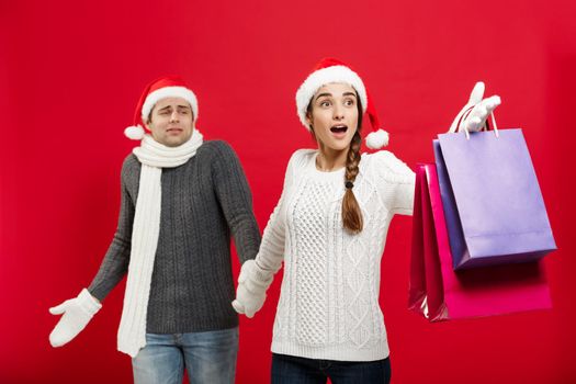 Christmas Concept - Beautiful girlfriend force her boyfriend to go shopping over red christmas background.