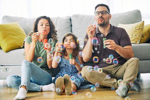 Family having fun blowing soap bubbles on sofa at home