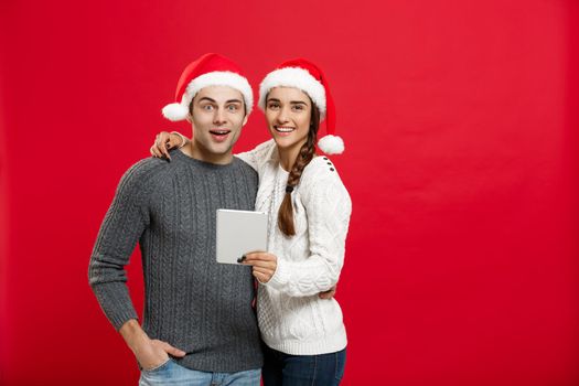 Christmas Concept - Young handsome and beautiful couple enjoy playing on tablet in christmas day.