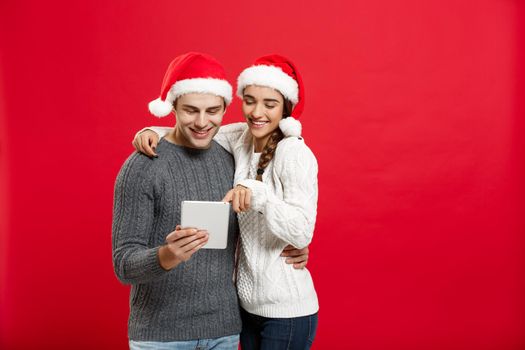 Christmas Concept - Young handsome and beautiful couple enjoy playing on tablet in christmas day.