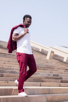 vertical photo of a stylish african man walking down a city staircase with his jacket over his shoulder, urban lifestyle concept, copy space for text