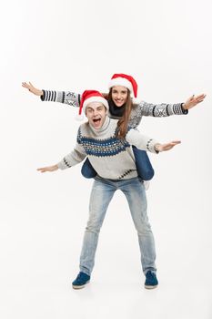 Christmas Concept - Full-length Young happy couple in sweaters enjoying piggyback ride isolated on white grey background.