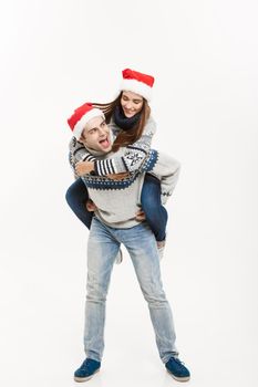 Christmas Concept - Full-length Young happy couple in sweaters enjoying piggyback ride isolated on white grey background.