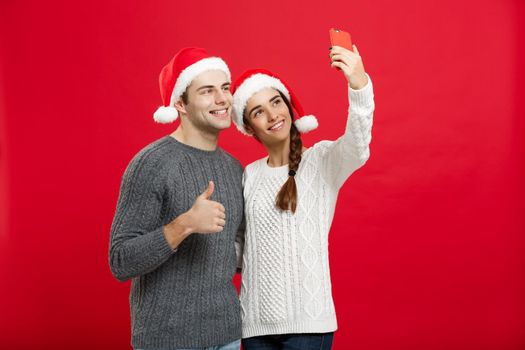 Christmas Concept - Young attractive couple taking a selfie by mobile phone celebrating in Christmas day.