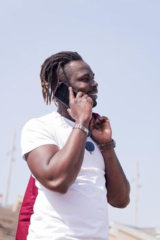 vertical photo of a smiling african man walking while talking by phone, concept of technology and city lifestyle, copy space for text