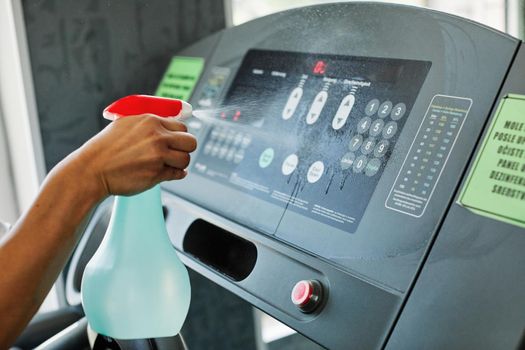 Young woman cleaning and weeping fitness gym equipment with sprayer