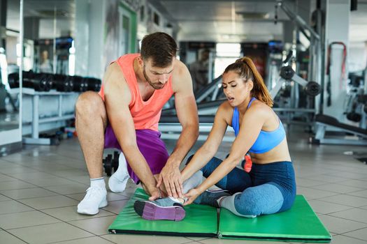 Sportswoman with personal trainer in gym. Sports woman having injury leg