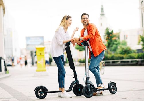 Young couple having fun driving electric scooter through the city