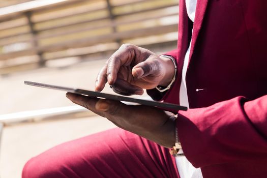 detail of the hands of a black man using a tablet outdoors in the city, technology and remote work concept