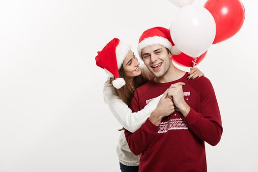 Christmas Concept - Young girlfriend holding balloon is hugging and playing with her boyfriend doing a surprise on Christmas.