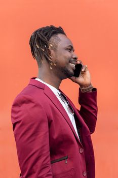 vertical profile portrait of a stylish black businessman in suit smiling and talking on phone in front of red background, copy space for text, concept of technology and communication