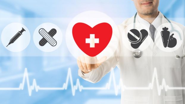 Doctor pointing at heart symbol icon on blue hospital background. Medical and healthcare concept.