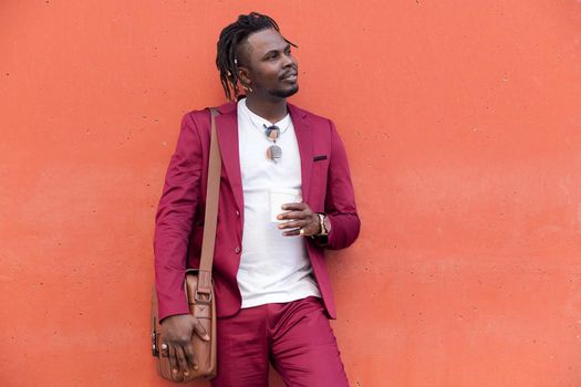 portrait of a stylish african businessman dressed in suit with briefcase holding coffee in his hand in front of red background, copy space for text