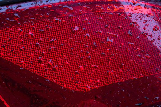 Close-up of the red tail light of a modern car with raindrops.