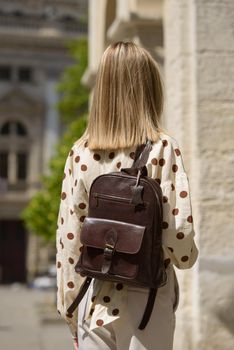 Woman with a brown leather backpack with antique and retro look. Outdoors photo.