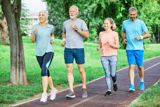 Smiling active senior people jogging together in the park
