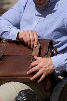 Man with a brown leather briefcase with antique and retro look. Outdoors photo.