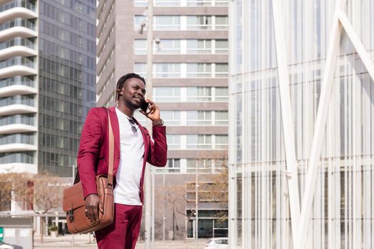 elegant black businessman with briefcase walks through the city financial downtown talking on phone, concept of technology and communication, copy space for text