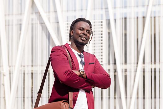elegant black businessman with briefcase posing with arms folded in the financial downtown of the city, copy space for text