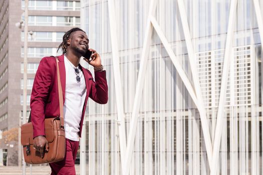 smiling black businessman with briefcase walks through the city financial downtown talking on phone, concept of technology and communication, copy space for text