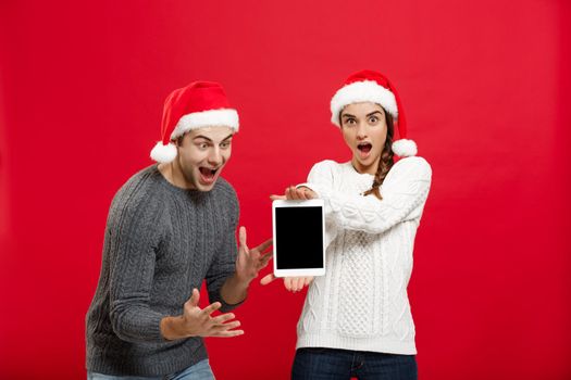 Christmas concept - Happy young couple in christmas sweaters surprising something in digital tablet.