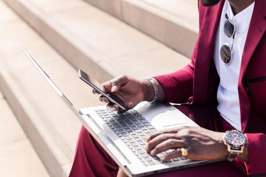 detail of the hand of an unrecognizable businessman using a smart phone and computer laptop, technology and remote work concept, copy space for text