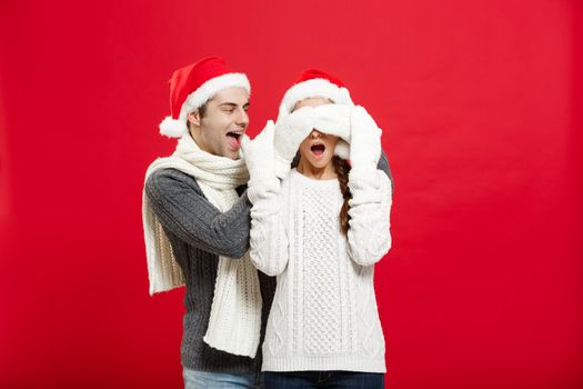 Christmas concept - Portrait of a romantic young boyfriend surprising girlfriend over red studio background