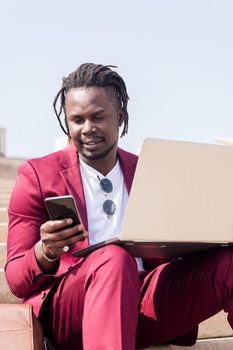 vertical photo of a stylish african businessman working outdoors with laptop and smart phone, technology and remote work concept, copy space for text
