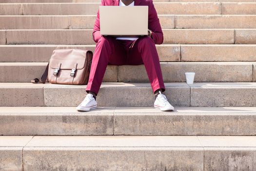 unrecognizable man working on his laptop computer sitting on a city staircase, technology and remote work concept