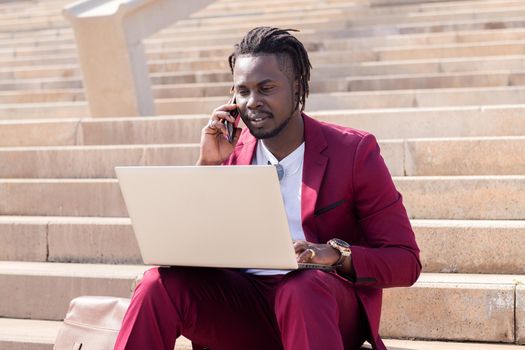 african man working with computer laptop and phone sitting on city stairs, concept of technology and remote work