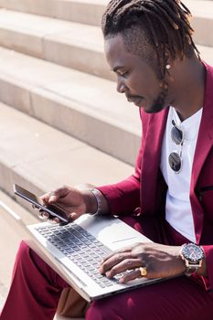 vertical photo of a black businessman using a smart phone and computer laptop, technology and remote work concept, copy space for text