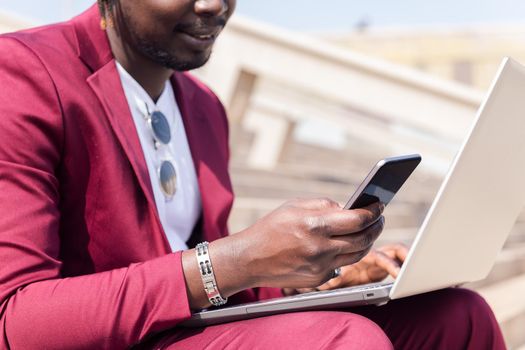 unrecognizable black businessman using a smart phone and computer laptop, technology and remote work concept, copy space for text