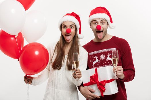 Christmas Concept - Young caucasian couple holding gifts,champagne and balloon making funny face on Christmas.