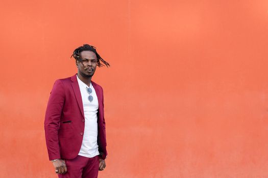 black businessman in suit with afro hair blowing in the wind poses in front of a red background, copy space for text