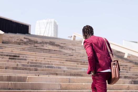 rear view of an unrecognizable black businessman walking up some city stairs with his briefcase, concept of business and city lifestyle, copy space for text
