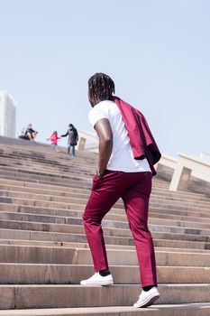 stylish black man walking up a city staircase with his blazer over his shoulder, urban lifestyle concept, copy space for text