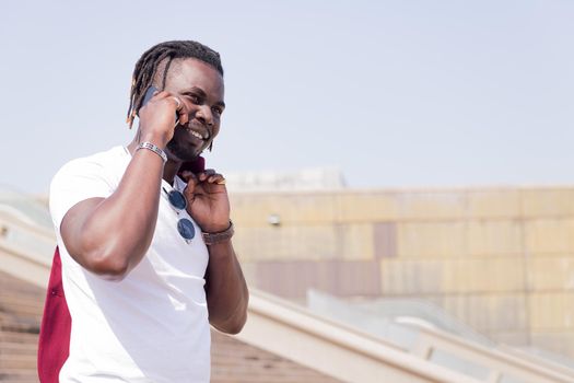 smiling african man walking down a city staircase talking by phone, concept of technology and city lifestyle, copy space for text