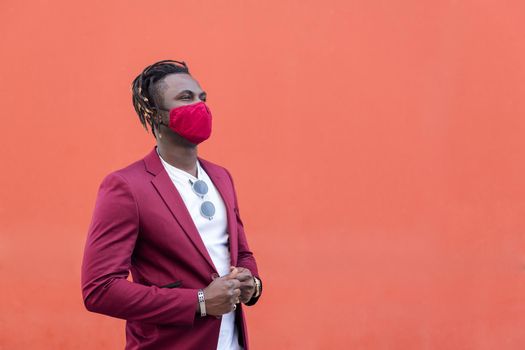 elegant african man with protective mask to match his suit on a red background, copy space for text, concept of elegance and fashionable lifestyle
