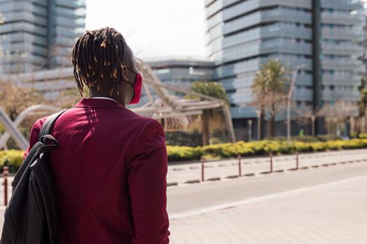 rear view of a black businessman walking around the city with a red mask to match his suit, concept of elegance and fashionable lifestyle, copy space for text