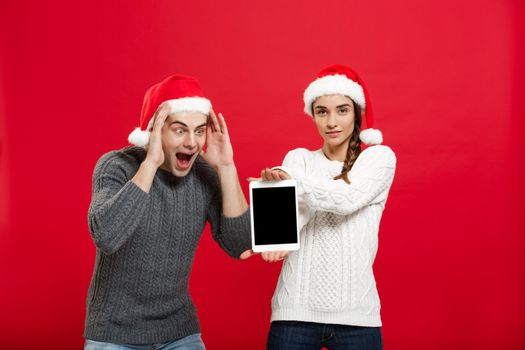 Christmas concept - Happy young couple in christmas sweaters surprising something in digital tablet.