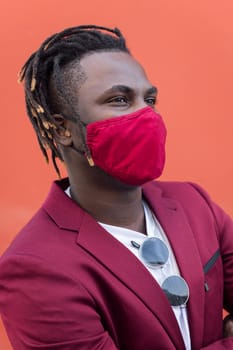 vertical portrait of a stylish african man with protective mask to match his suit on a red background, concept of elegance and fashionable lifestyle