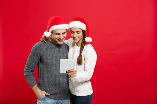 Christmas Concept - Young handsome and beautiful couple enjoy playing on tablet in christmas day.