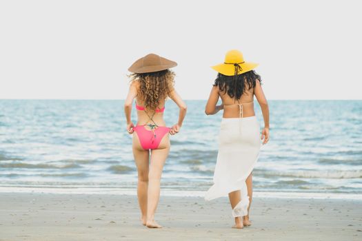 Happy women in bikinis go sunbathing together on tropical sand beach in summer vacation. Travel lifestyle.