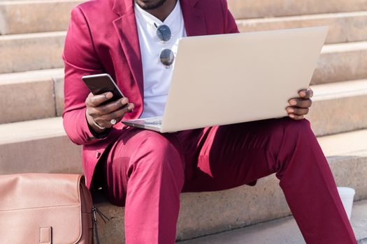 unrecognizable elegant black businessman working outdoors with laptop and smart phone, technology and remote work concept